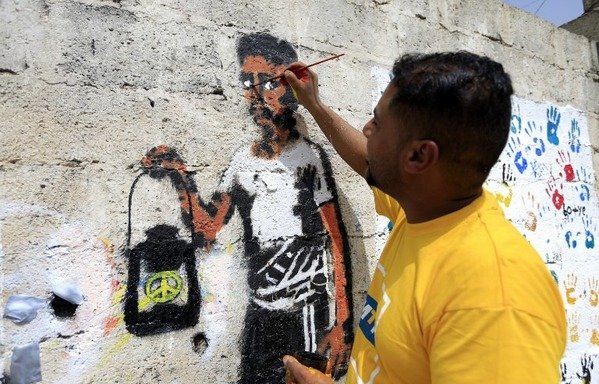 A Yemeni artist paints a pro-peace graffiti on a wall in the capital Sanaa on August 16th, of a man holding a lantern with a peace sign in it. [Mohammed Huwais/AFP]  