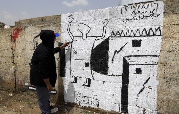 Un artiste yéménite peint un graffiti qui appelle à la fin de la guerre au Yémen en montrant un homme blessé lors d'une frappe aérienne. [Mohammed Huwais/AFP]