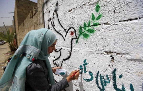 A Yemeni artist paints the peace symbol of a dove holding an olive branch on a wall in the capital Sanaa on August 16th. [Mohammed Huwais/AFP]
