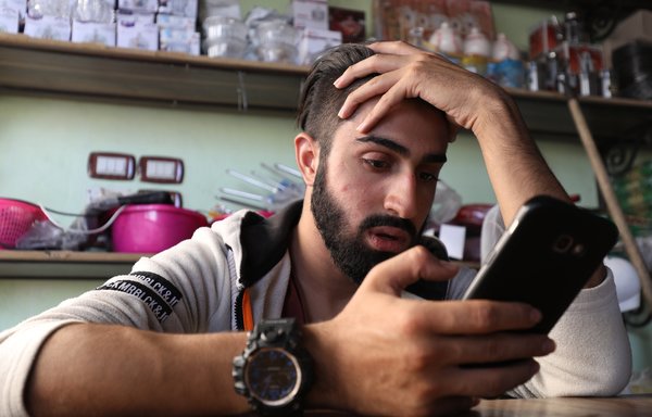 As he works at his father's shop in Maaret al-Numan, Syrian rapper Amir al-Muarri listens to his favourite artists on his telephone. [Omar Haj Kadour/AFP] 