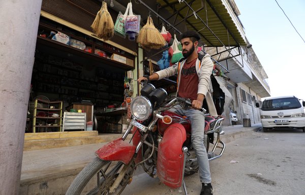 Al-Muarri parks his motorcycle in front of his father's shop in Maaret al-Numan. [Omar Haj Kadour/AFP]