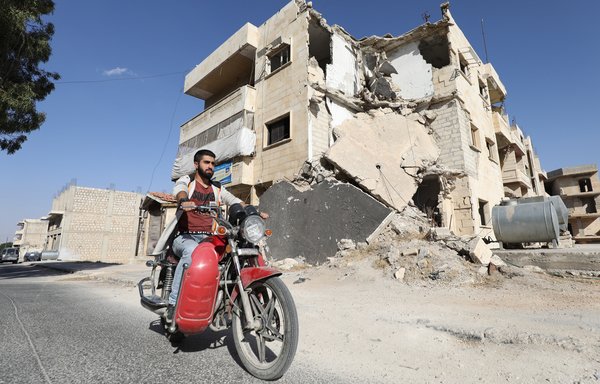 Bombed-out buildings form the backdrop of al-Muarri's life. Here he rides his motorcycle through a damaged street in Maaret al-Numan. [Omar Haj Kadour/AFP] 