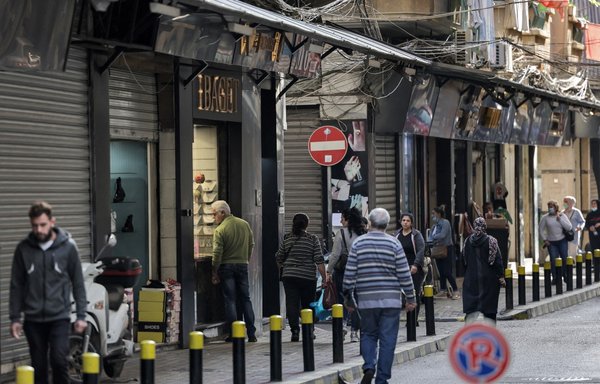 أشخاص يسيرون أمام متاجر مغلقة أو نصف مفتوحة في سوق برج حمود الشعبي في بيروت، يوم 14 كانون الأول/ديسمبر. [جوزيف عيد/وكالة الصحافة الفرنسية]