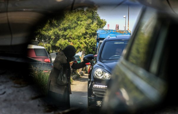 صورة ملتقطة يوم 14 كانون الأول/ديسمبر عبر مرآة سيارة جانبية لمتسولة تستجدي المال من سائق سيارة في خضم حركة المرور في بيروت. [جوزيف عيد/وكالة الصحافة الفرنسية]