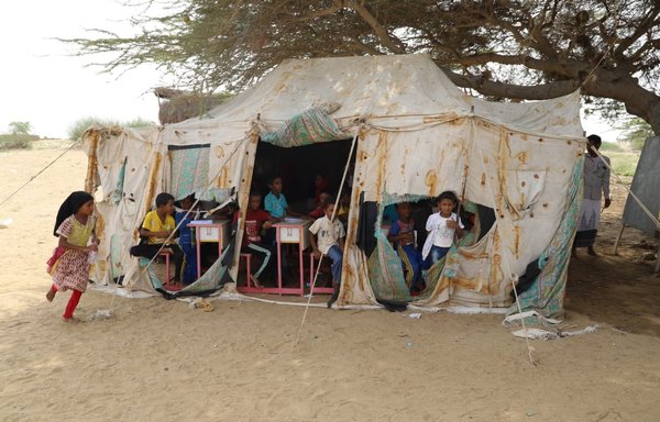 در اردوگاه آوارگان الرحبه در جبل حبشی واقع در استان تعز، کودکان در یک کلاس درس صحرایی سر میزشان نشسته‌اند. [واحد اجرایی آوارگان داخلی]