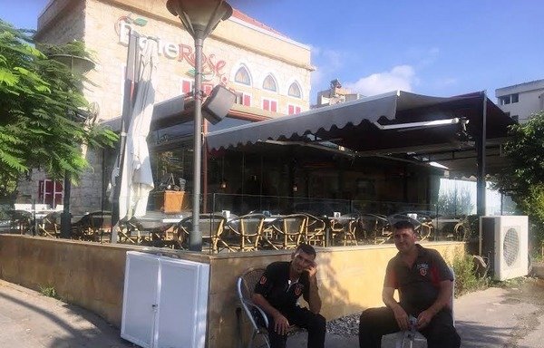 عاملان في مطعم في أنطلياس ببيروت يجلسان في الخارج بانتظار الزوار. عانى قطاع السياحة من الاعتداءات الإرهابية التي شنتها مجموعات متطرفة والحرب المستمرة في سوريا. [نهاد طوباليان/المشرق]