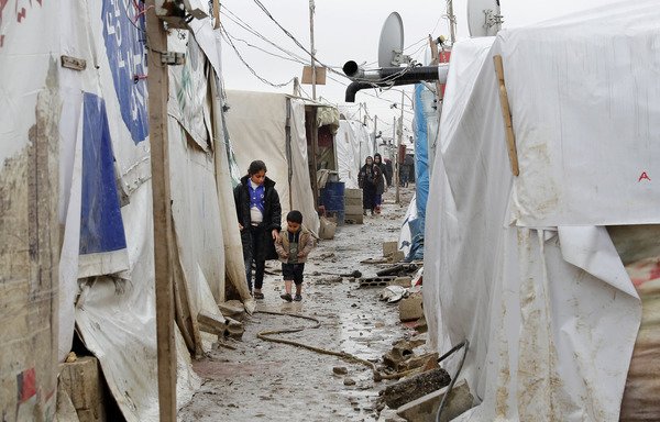 أطفال لاجئون سوريون يسيرون في زقاق موحل في مخيم غير شرعي للاجئين بقرية دير زنون البقاعية في 31 كانون الثاني/يناير. [جوزيف عيد/وكالة الصحافة الفرنسية]