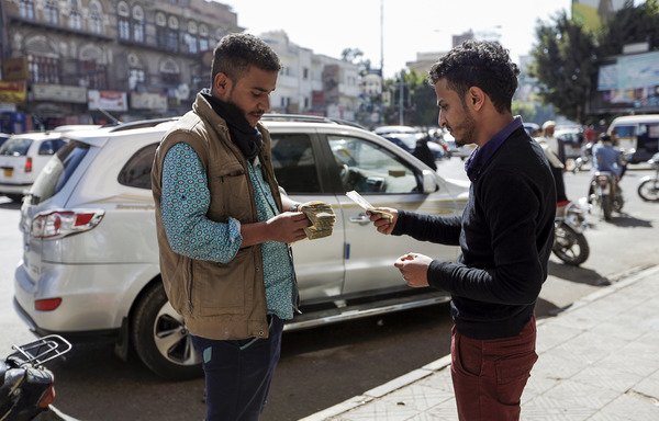 A Yemeni man counts a stack of Yemeni rials as another prepares to give him US dollar notes on a street in Sanaa, on February 12th. [Mohammed Huwais/AFP]