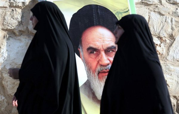 Des Libanaises passent devant le portrait du fondateur de la République islamique d'Iran, l'Ayatollah Rouhollah Khomeini, dans la ville de Saksakieh, dans le sud du Liban le 27 novembre 2015, pendant la cérémonie funéraire d'Ali Tanana, qui aurait trouvé la mort lors de batailles à Alep en Syrie en combattant aux côtés du Hezbollah, la milice chiite du Liban. [Mahmoud Zayyat/AFP]