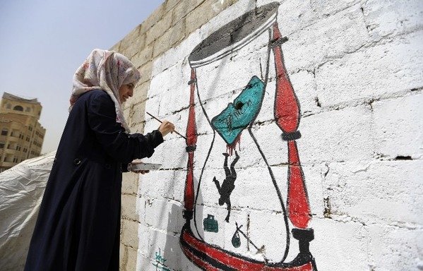 Un artiste yéménite peint un sablier qui montre des individus tombant dans le conflit en cours dans le pays. [Mohammed Huwais/AFP]