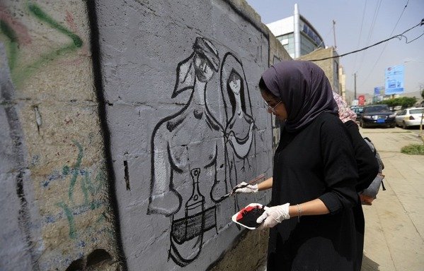A graffiti on a wall in Sanaa shows a man and a woman in traditional garb with a dove between them. [Mohammed Huwais/AFP]
