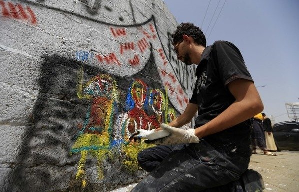 Un graffiti représentant des Yéménites en habits colorés s'abritant sous une tente décore un mur de Sanaa parmi d'autres fresques appelant à la paix et à la tolérance et rejetant la guerre. [Mohammed Huwais/AFP]
