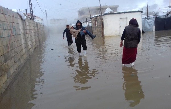 A man carries a child through the floodwater at Bar Elias camp. [Photo courtesy of Sawa for Development and Aid]