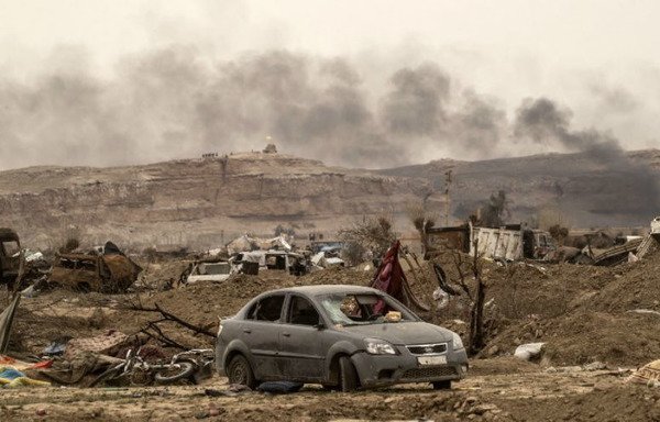 This picture taken on March 24th shows smoke rising behind destroyed vehicles and damaged buildings in the village of al-Baghouz, a day after ISIS lost its last holdout in Syria. [Delil Souleiman/AFP]