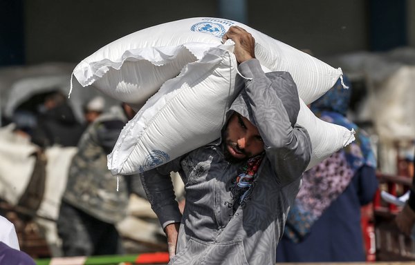 Un homme palestinien porte sur son épaule un sac de farine reçu du centre de distribution de l'UNRWA dans le camp pour réfugiés de Rafah au sud de la Bande de Gaza le 17 novembre. [Said Khatib/AFP]