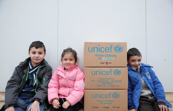Children sit next to UNICEF winter aid for refugees in Lebanon's Bekaa Valley. [UNICEF]