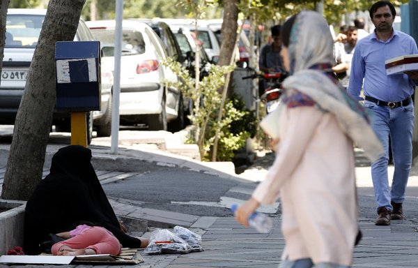 یک زن در تاریخ ۳۱ ژوئیه ۲۰۱۸ در تهران، پایتخت ایران، از کنار یک گدا عبور می‌کند. [عطا کناره/ خبرگزاری فرانسه]