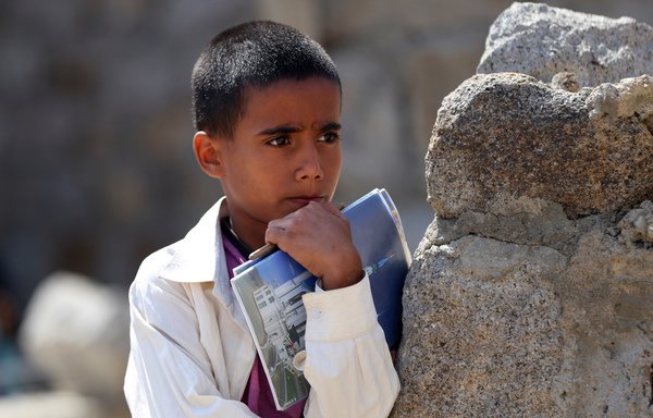 A Yemeni boy holds his notebooks at an open-air class near an unfinished school on September 16th, 2019, in the south-western village of al-Kashar in Taez province's Mashraa and Hadnan district. [Ahmad al-Basha/AFP]
