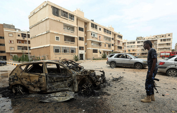 A fighter loyal to Libya's UN-recognised Government of National Accord stands next to a destroyed car following bombardment earlier by forces from strongman Khalifa Haftar, who is supported by Russia's Wagner Group, in Tripoli on May 9th. [Mahmud Turkia/AFP]
