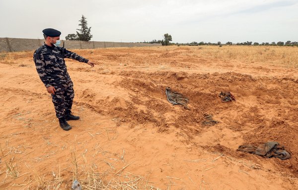 A member of security forces affiliated with the Libyan Government of National Accord (GNA)’s Interior Ministry points at the reported site of a mass grave in Tarhuna, about 65km southeast of the capital, Tripoli, on June 11. [Mahmud TURKIA/AFP]