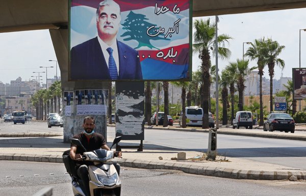 Un homme à moto passe devant un panneau d’affichage portant une affiche représentant le Premier ministre libanais assassiné Rafic al-Hariri dans une rue de Sidon, sa ville natale, le 18 août. [Mahmoud Zayyat/AFP]