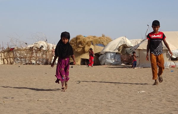 أطفال يمنيون يمشون أمام خيام في مخيم للنازحين في مديرية الخوخة بالحديدة في 6 أيار/مايو. [خالد زياد / وكالة الصحافة الفرنسية]