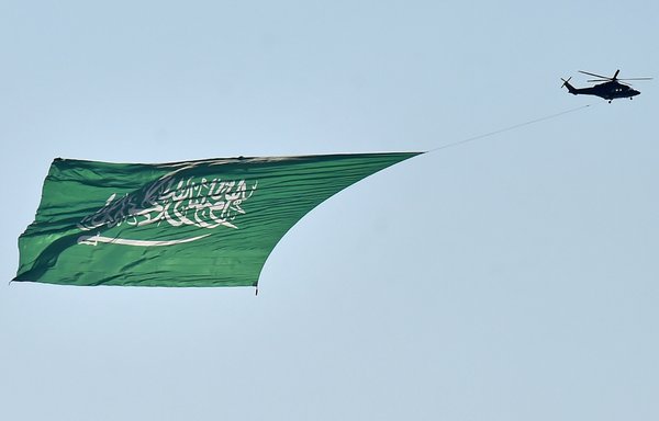 A military helicopter, carrying a huge national flag, flies over Riyadh during celebrations marking Saudi Arabia's 90th National Day on September 23rd. [Fayez Nureldine/AFP]