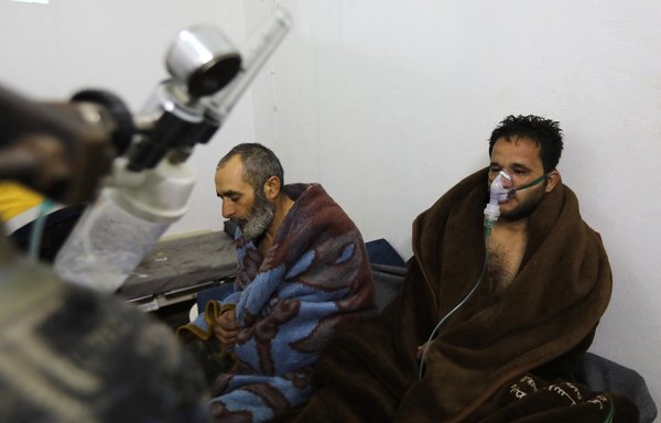 Syrians reportedly suffering from breathing difficulties following Syrian regime airstrikes on the Idlib town of Saraqeb rest around a stove at a field hospital in a village on the outskirts of Saraqeb on February 4, 2018. [Omar Haj Kadour/AFP]