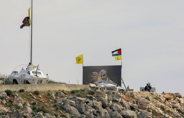 A picture taken from the Israeli border town of Metula shows Lebanese nationals sightseeing next to a billboard of slain Iraqi PMF deputy Abu Mahdi al-Muhandis and IRGC commander Qassem Soleimani, while UNIFIL soldiers watch, on January 2. [Jalaa Marey/AFP]