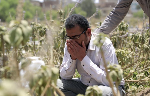 روز ۱۹ فروردین یکی از خویشاوندان یک مرد یمنی که بر مزار همسرش حضور یافته، او را آرام می کند. همسر این مرد آبستن بود و از مشکلات تنفسی رنج می برد. وی پس از آن که سه بیمارستان در صنعا، که تحت کنترل حوثی ها است، به دلیل ترس از آلوده بودنش به ویروس کرونا از پذیرش او خودداری کردند، درگذشت. [محمد هویس/ خبرگزاری فرانسه]