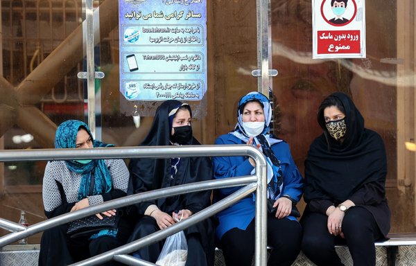 Iranian women wearing protective masks against COVID-19 wait at a bus station in Tehran on May 16. Most average Iranians are still not vaccinated. [Atta Kenare/AFP]