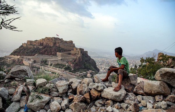 پسری در روز ۲۷ تیر ماه در آستانۀ فرا رسیدن عید قربان، به پرچم غول‌پیکر یمن در حال اهتزاز در ارگ تاریخی القاهره به جامانده از قرن ۱۲ در شهر تعز، سومین شهر یمن خیره شده است. [احمد الباشا/ خبرگزاری فرانسه]