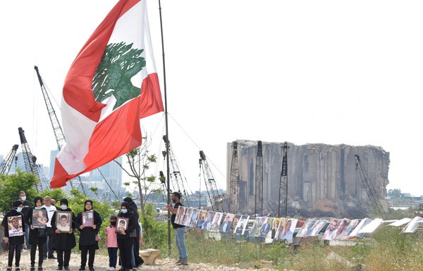 Holding photos of the loved ones they lost in the Beirut port blast, family members raise the Lebanese flag near the explosion site. [Ziad Hatem]