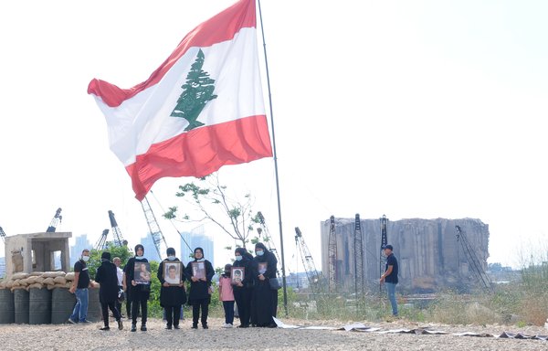 The families of the victims of the Beirut port explosion stand beneath the Lebanese flag near the port's main entrance during a vigil on July 4. [Ziad Hatem/Al-Mashareq]