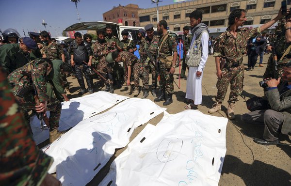 An armed man takes a 'selfie' picture as others surround body bags containing the corpses of nine men who were executed in a public square in Sanaa on September 18. [Mohammed Huwais/AFP]