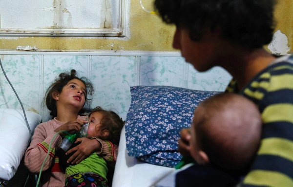 A Syrian girl holds an oxygen mask over the face of an infant at a make-shift hospital following a reported gas attack on Douma on January 22, 2018. [Hasan Mohamed/AFP]