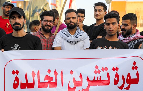 متظاهرون يقفون خلف لافتة كتب عليها ʼثورة تشرين الخالدةʻ فيما يحتشدون في ساحة الحبوبي في الناصرية يوم 25 تشرين الأول/أكتوبر للاحتفال بالذكرى السنوية الثانية للحراك الاحتجاجي الذي انطلق في تشرين الأول/أكتوبر 2019. [أسعد نيازي/وكالة الصحافة الفرنسية]