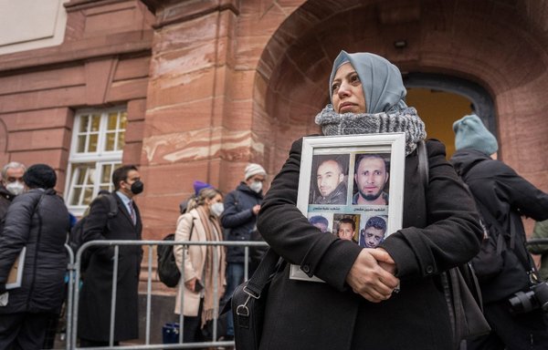 A Syrian campaigner of the Caesar Families Association, Yasmen Almashan, holds pictures of victims of the Syrian regime as she and others wait outside the courthouse where former Syrian intelligence officer Anwar Raslan is on trial in Koblenz, western Germany, on January 13. [Bernd Lauter/AFP]