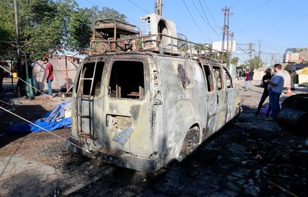 Iraqis look at a burnt broadcasting van for a local TV station at a protest camp for supporters of the PMF in Baghdad, on November 6, a day after clashes with the police during a demonstration to express rejection of the parliamentary election results. [Ahmad al-Rubaye/AFP]