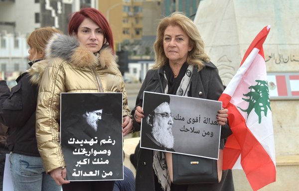 تظاهرکنندگان ۱۳ اسفند، مقابل مجسمه مهاجر لبنانی در نزدیکی بندر بیروت جمع شده‌اند و پلاکاردهایی در دست دارند که حزب‌الله را مقصر بحران کنونی لبنان معرفی می‌کند. [زیاد حاتم/المشارق]