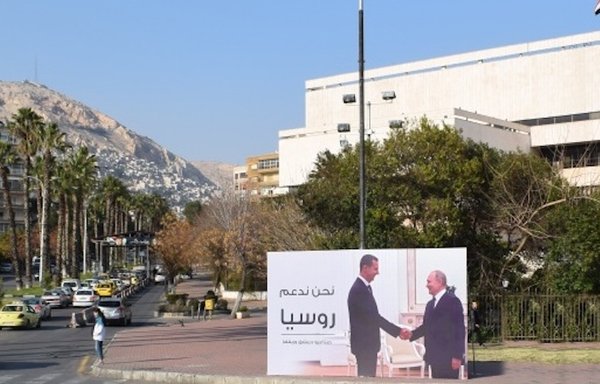 روی بیلبوردی در دمشق با عنوان «ما از روسیه حمایت می‌کنیم»، عکس رؤسای جمهوری سوریه و روسیه دیده می‌شود که دست می‌دهند و حمایت رژیم سوریه از جنگ روسیه در اوکراین را به نمایش می‌گذارند. [اتاق صنایع دمشق]