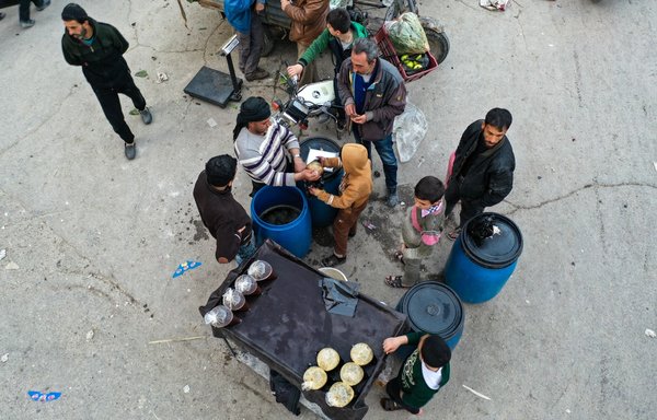 این تصویر سوری‌هایی را نشان می‌‌دهد که روز ۲۶ فروردین ۱۴۰۰ قبل از افطار در بازاری در شهر اریحه، واقع در جنوب ادلب، غذا خریداری می‌کنند. [عمر حاج قدور/ خبرگزاری فرانسه]
