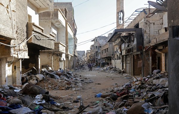 People walk amid rubble of destroyed buildings on a street in the Tadamon neighbourhood of southern Damascus on November 3, 2018. [Louai Beshara/AFP]