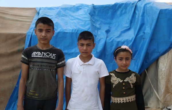 Ali, Ahmed and Fada Ibrahim Sultan pose for a photo in al-Tah displacement camp, where they live with their mother, Rasha Muhammad al-Rasheed. [Ali Haj Suleiman]