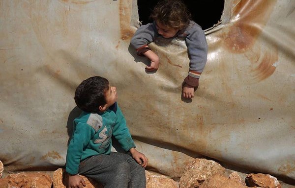 A Syrian child talks to another from inside a tent in a displacement camp. [Ali Haj Suleiman]