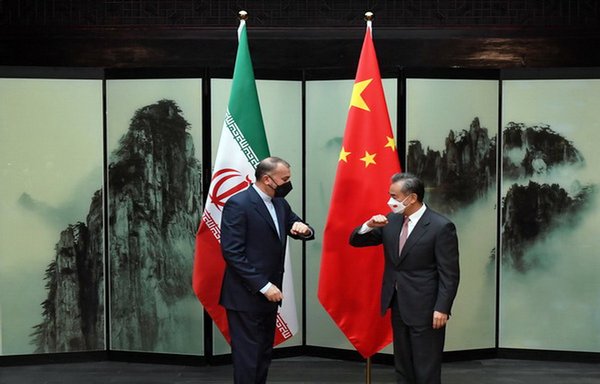 وانگ یی، وزیر امور خارجۀ چین، و حسین امیرعبداللهیان، همتای ایرانی وی، در جریان دیدارشان در روز ۱۱ فروردین آرنج‌‌هایشان را (به نشانۀ دست‌دادن) به‌هم می‌زنند. [وبسایت وزارت امور خارجۀ چین]