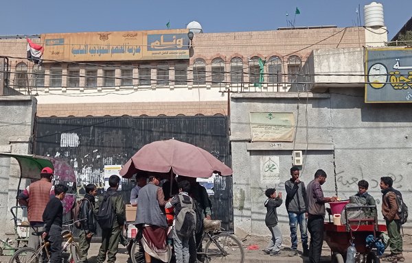 طلاب يشترون وجبات خفيفة من بائع خارج مدرسة المعتصم للبنين بأمانة العاصمة صنعاء في كانون الأول/ديسمبر. [هيثم محمد/ المشارق]