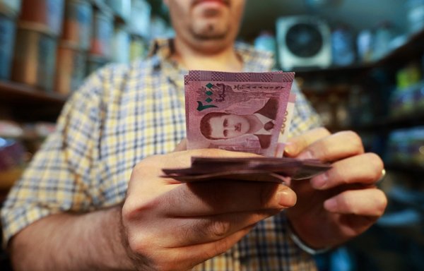 A merchant counts Syrian pound notes, bearing a portrait of the Syrian President Bashar al-Assad, at the Bzourieh market in Damascus on September 11, 2019. [Louai Beshara/AFP]