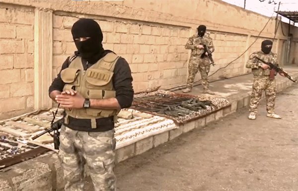 SDF fighters stand with weapons, explosives and explosive belts seized during Operation al-Jazeera Thunderbolt in January. [SDF Press Centre]