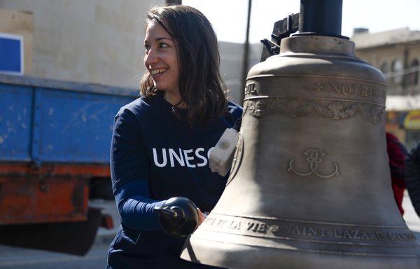 A woman poses next to one of three bells as they are prepared for installation on February 28 in the bell tower of the historic Church of Our Lady of the Hour in Mosul. [Zaid al-Obeidi/AFP]